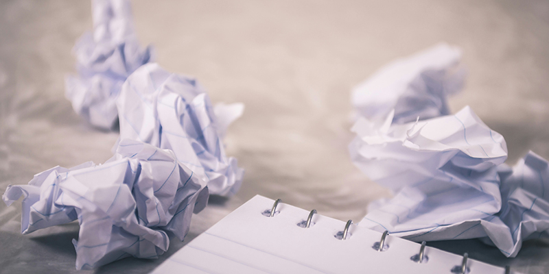 A single piece of crumpled white paper sitting on a dark wooden table, representing the trial and error of the writing process.