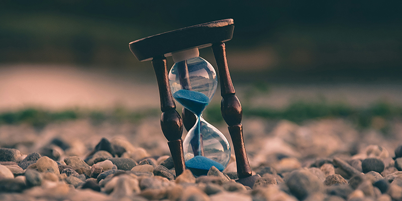 An hourglass sitting on a bed of stones, with sand running through the middle, symbolizing time constraints in research.